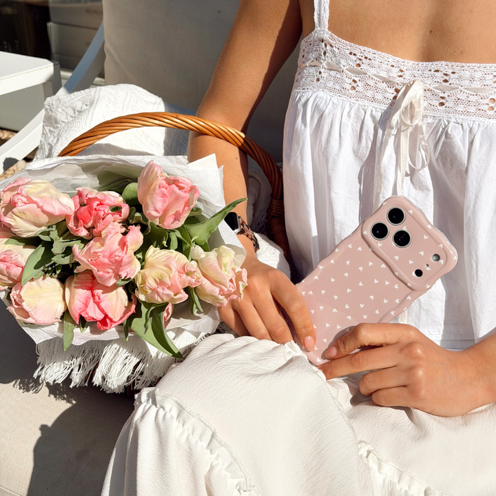 Girl posing with flowers in a basket holding the Wavy Chai Hearts Phone Case