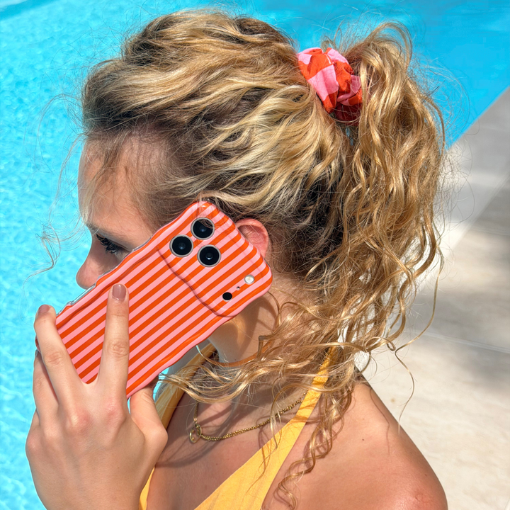 Woman holding a phone with a pink and orange case by a pool