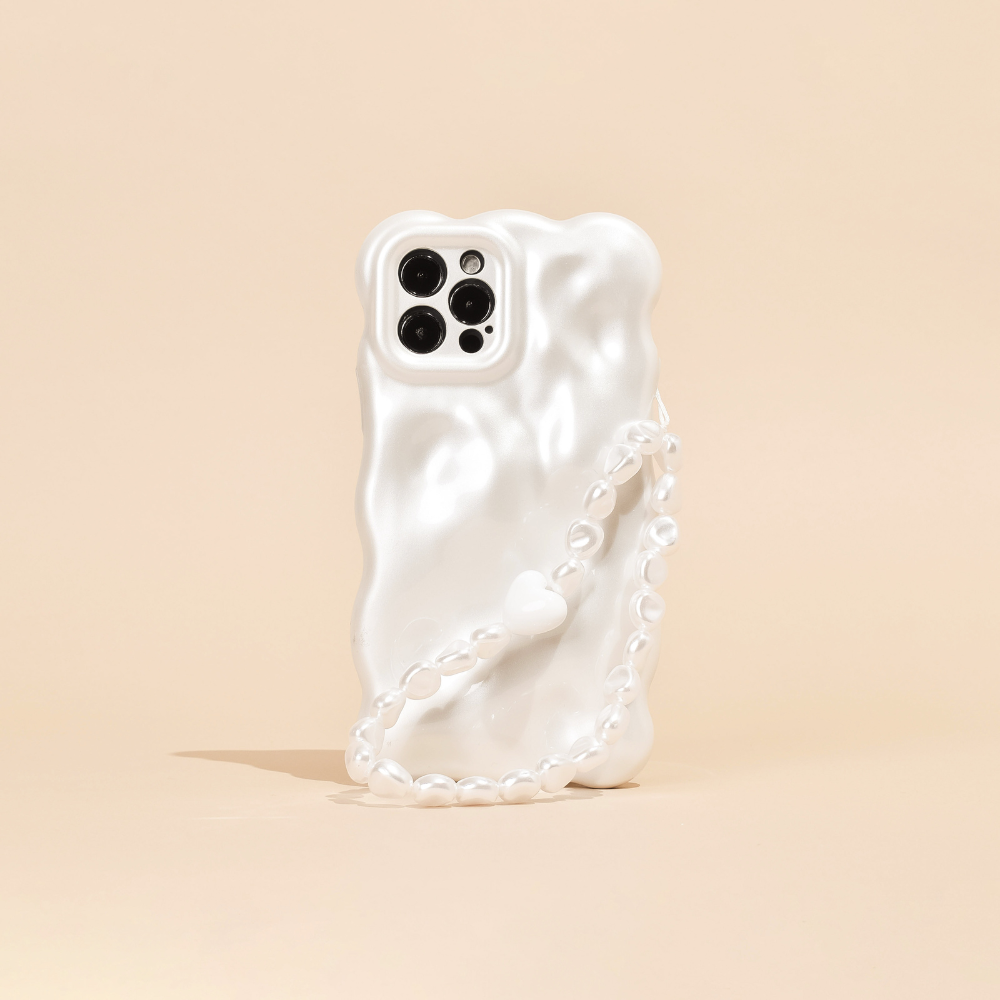 A white, wavy-textured phone case is shown standing on a light beige surface, featuring Coconut Lane's Beaded Phone Strap - Chunky Pearls. The phone's camera section with multiple lenses is visible, contributing to a sleek and modern aesthetic.