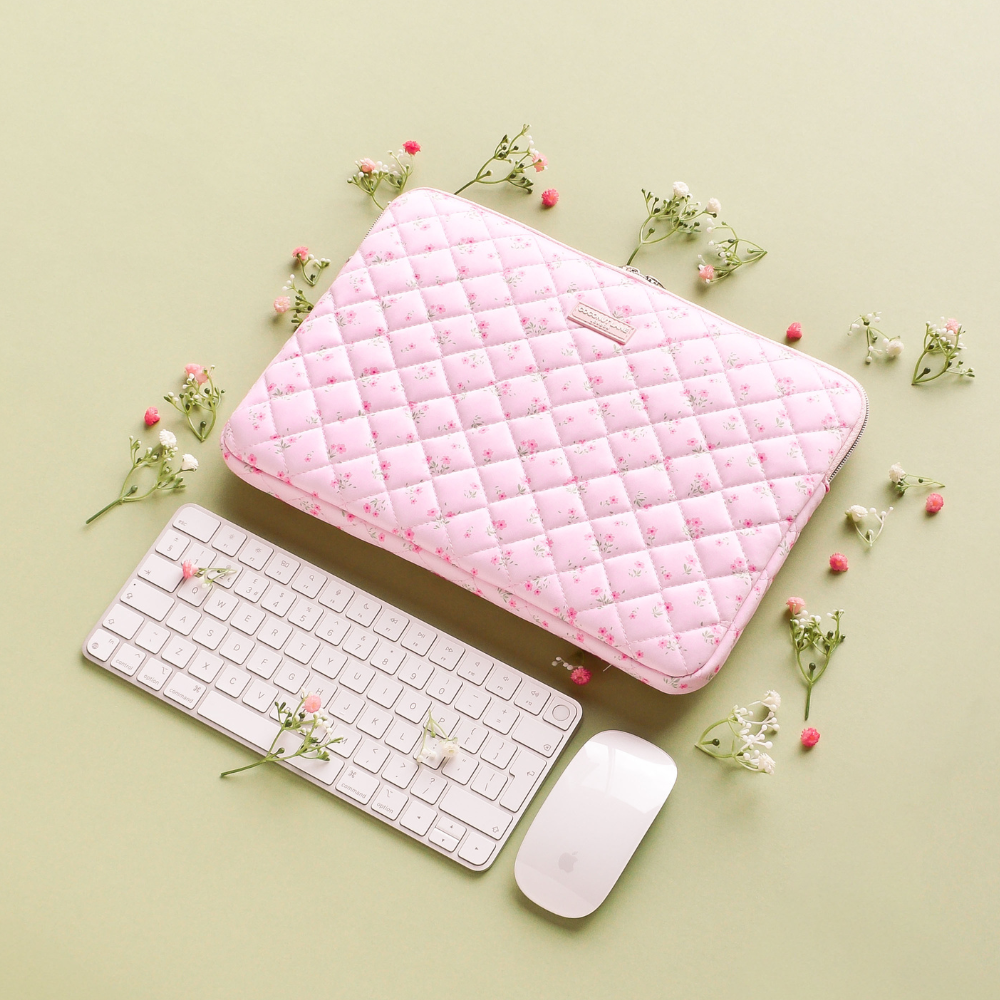 Pink quilted floral laptop sleeve beside a white keyboard and mouse on a green background.