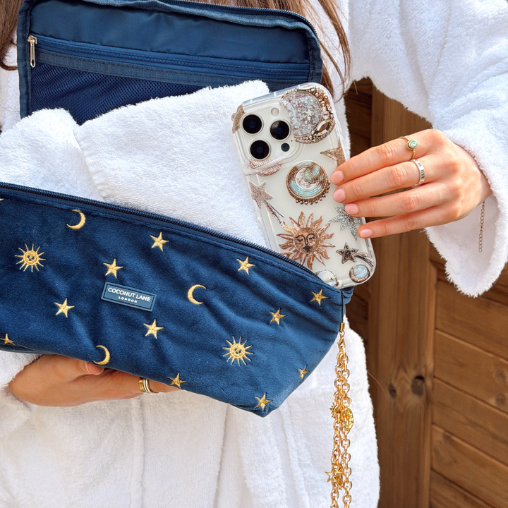Girl holding pastel celestial phone case next to vanity case wearing white dressing gown in sauna