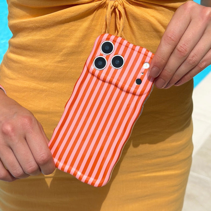 Phone case with orange and pink striped pattern held by a person against a yellow dress, standing by pool