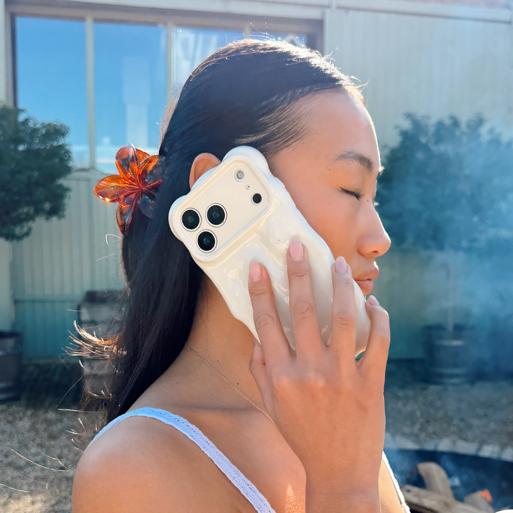 Woman outdoors with eyes closed, wearing a tortoiseshell floral claw clip and holding a white phone.